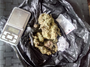 Na zdjęciu widoczny jest czarny worek foliowy, w którym znajduje się marihuana, zawiniątko z folii aluminiowej z marihuaną, torebka foliowa z kokainą oraz waga elektroniczna.
