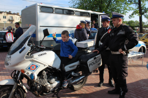 Na zdjęciu widoczny jest mały chłopiec siedzący na policyjnym motocyklu, przy nim stoi policjant z pruszkowskiej drogówki