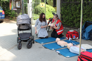 Na zdjęciu widoczny jest punkt pierwszej pomocy oraz młoda matka, która uczy się udzielać pierwszej pomocy niemowlakowi
