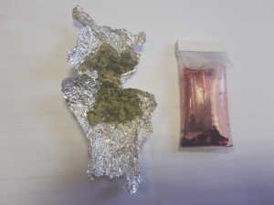 Na zdjęciu widoczne zawiniątko z foli aluminiowej z suszem roślinnym - marihuaną, obok widoczny jest tester narkotykowy.