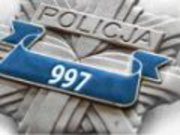 Na zdjęciu widoczna jest odznaka policyjna w kształcie gwiazdy koloru srebrnego, po środku widoczny jest niebieski pasek z białymi cyframi 997.