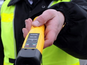 Na zdjęciu widoczna jest dłoń policjanta trzymająca urządzenie do badania zawartości alkoholu w wydychanym powietrzy alcoblow-koloru żółtego.