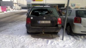 Na zdjęciu widoczny jest samochód marki volkswagen, który stoi zaparkowany na parkingu przy sklepie wielobranżownym. Pojazd ten jest koloru czarnego. Tylna szyna pojazdu jest uszkodzona w całości, wybita.