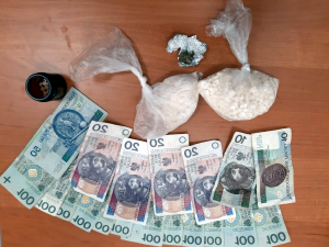 Na zdjęciu widoczne są dwa woreczki foliowe, szklana fifka, szklany brązowy pojemnik z tabletkami oraz banknoty o różnych nominałach. W szklanym brązowym pojemniku widoczne są tabletki koloru białego. W worku foliowym pierwszy od szklanego pojemnika widoczny jest biały proszek, który po badaniu okazał się być mefedronem. W drugim worku biała zbrylona substancja to amfetamina.
Pod workami widoczne są banknoty o różnych nominałach.