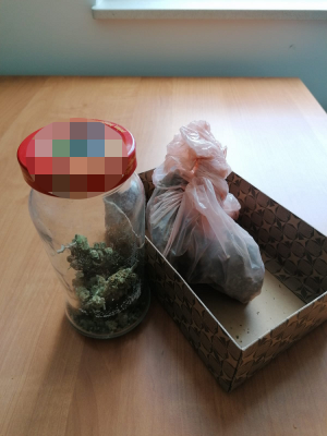 Na zdjęciu widoczny jest słoik szklany z zawatością marihuany oraz kartonowe pudełko, w którym jest torebka foliowa z marihuaną.