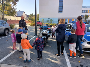 Policjanci pokazują przedszkolakom sprzęt policyjny radiowóz i motocykl.
