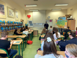 Na zdjęciu widoczny jest umundurowany policjant dzielnicowy z Michałowic, który rozmawia z uczniami w klasie.