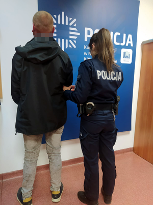 Na zdjęciu widoczna jest umundurowana policjantka, która prowadzi zatrzymanego za kradzież oleju napędowego mężczyznę. Mężczyzna ubrany jest w ciemną kurtkę i jasne spodnie.