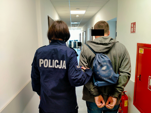 policjanta trzymająca za rękę zatrzymanego mężczyznę, stojący tyłem.