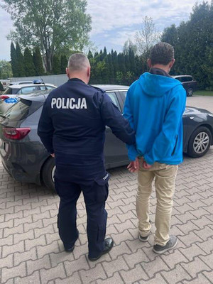 policjant umundurowany stojący tyłem, trzymający zatrzymanego mężczyznę