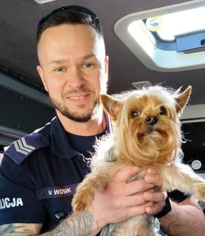 policjant umundurowany trzymający w rękach małego psa