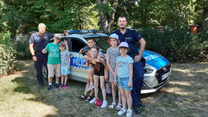 policjanci stoją obok oznakowanego radiowozu, obok dzieci