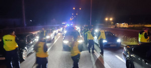 pojazdy oświetlone na ulicy, policjanci kontrolujący pojazdy. Czynności wykonywane w porze nocnej.