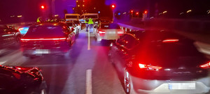 pojazdy oświetlone na ulicy, policjanci kontrolujący pojazdy. Czynności wykonywane w porze nocnej.