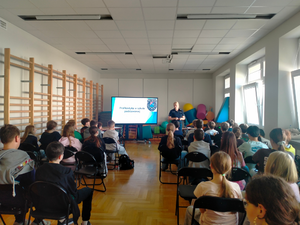 policjantka podczas spotkań profilaktycznych, widoczni uczniowie siedzący na krzesłach, słuchający umundurowanej policjantki