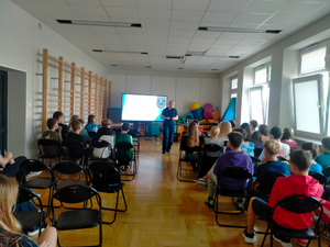 policjantka podczas spotkań profilaktycznych, widoczni uczniowie siedzący na krzesłach, słuchający umundurowanej policjantki