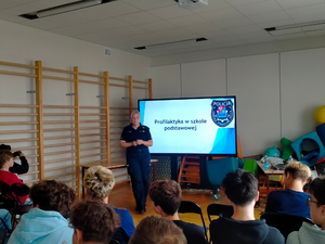 policjantka podczas spotkań profilaktycznych, widoczni uczniowie siedzący na krzesłach, słuchający umundurowanej policjantki