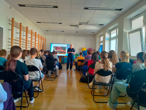 policjantka podczas spotkań profilaktycznych, widoczni uczniowie siedzący na krzesłach, słuchający umundurowanej policjantki