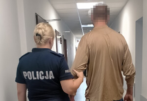 policjantka z zatrzymanym mężczyzną, toją tyłem na korytarzu