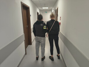 policjantka z zatrzymaną osobą, stoją tyłem na korytarzu