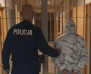 policjant z zatrzymanym mężczyzna stojący tyłem na tle krat